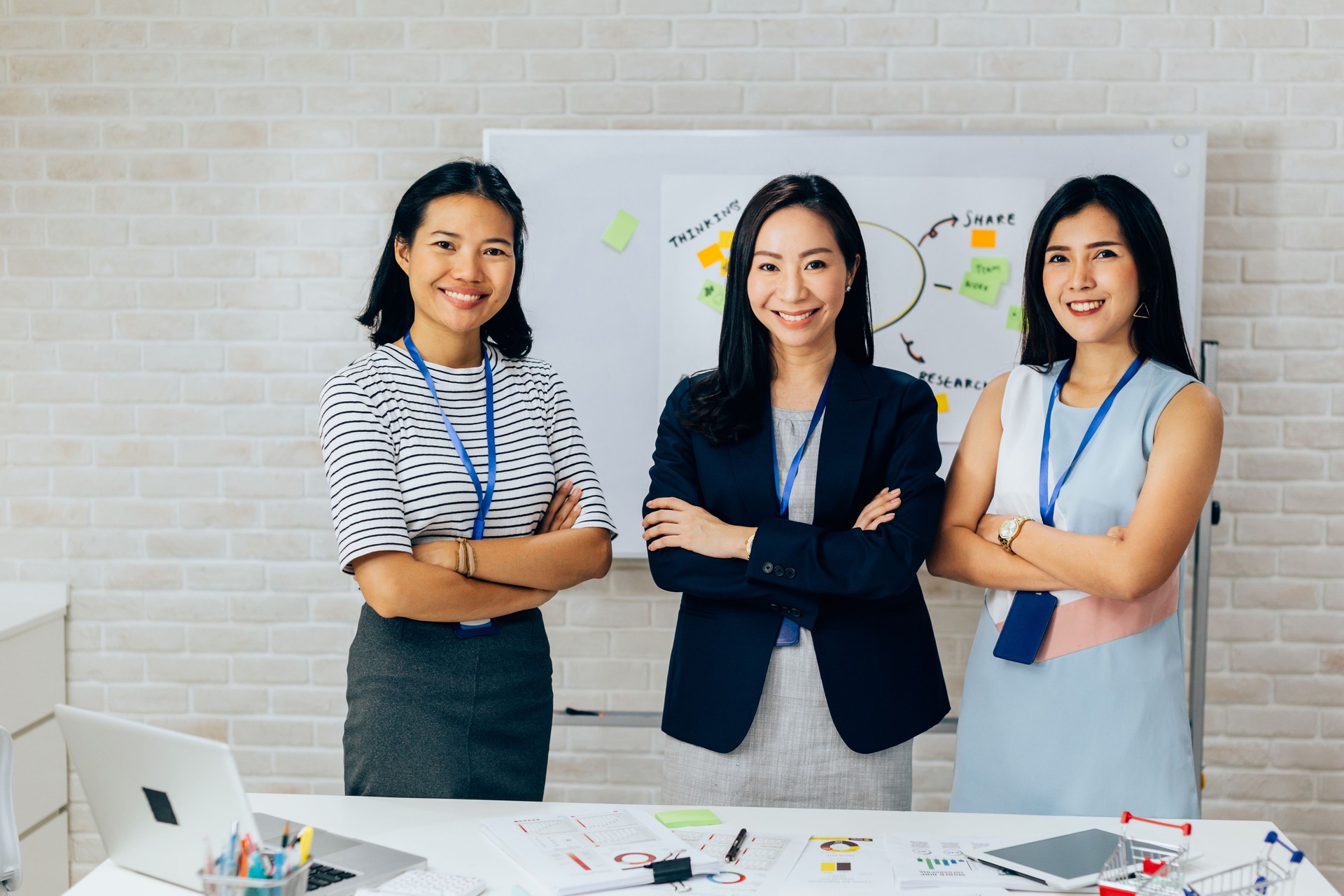 Smiling Asian young business women in casual wear standing in line with arms folded in meeting room